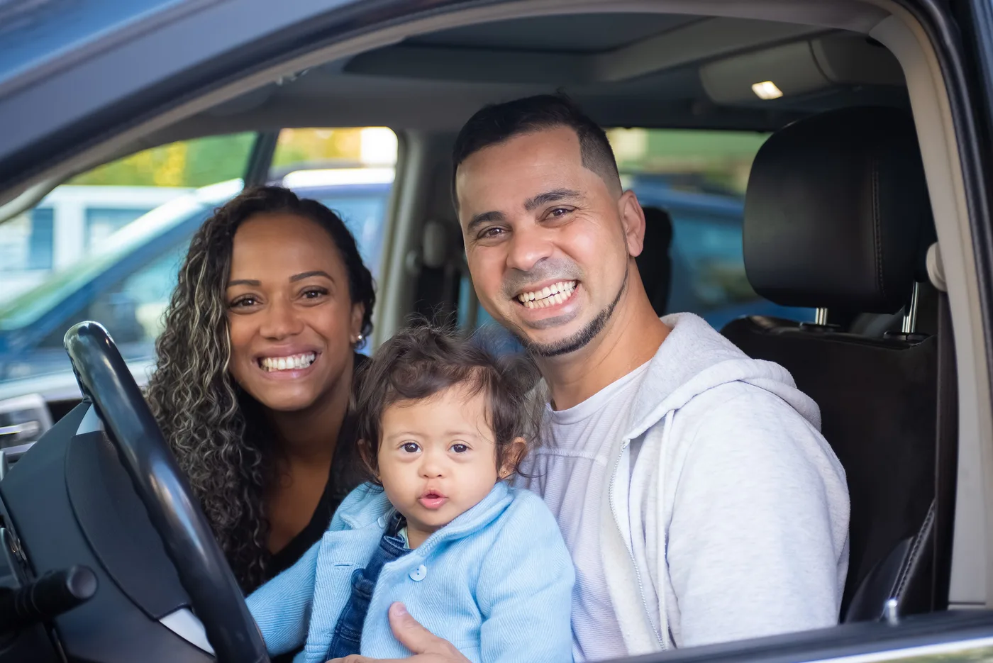 Smiling parents with their baby in the front seat of their car.