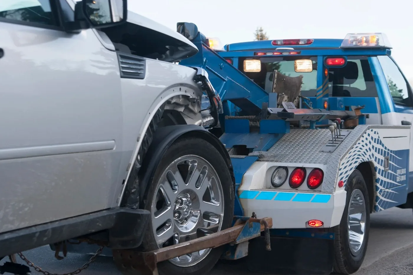 A white car lifted onto the back of a blue tow truck.