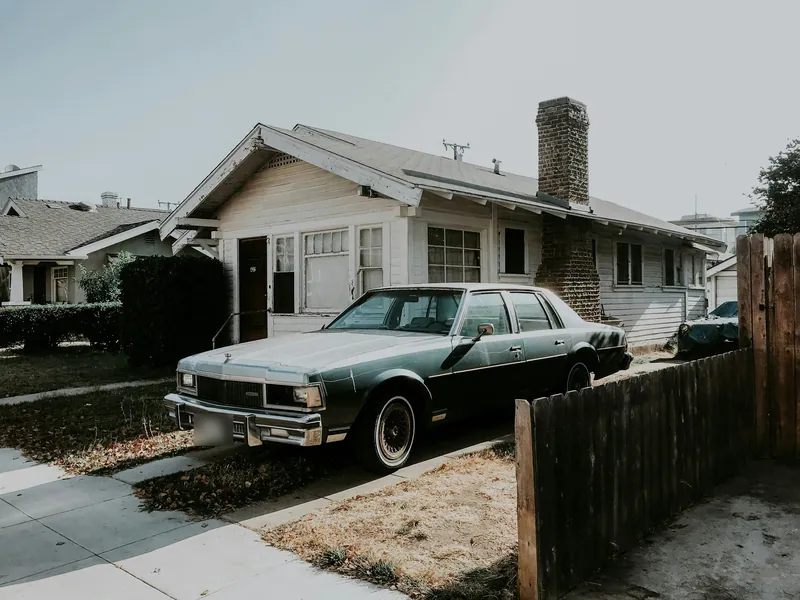 An older blue sedan parked in the driveway of a family home.