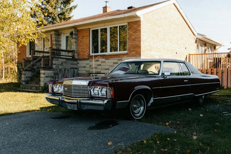 A burgundy vintage car parked in a sunlit residential driveway.