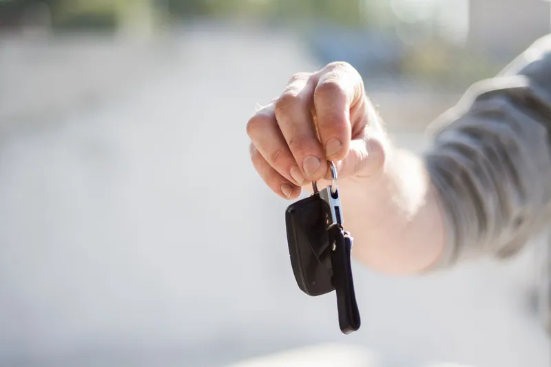 A hand holding out a car key on its ring.