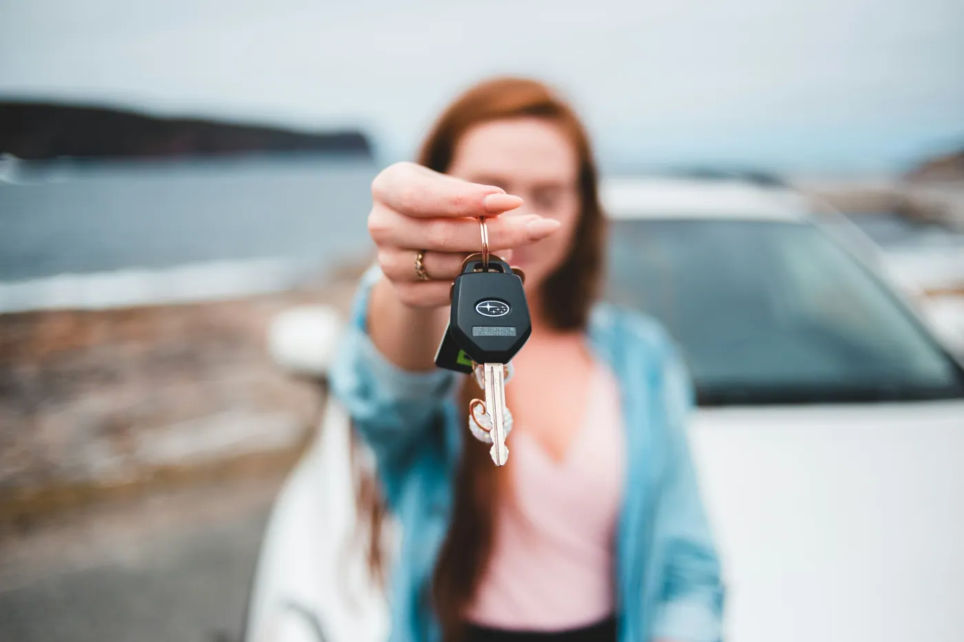 A woman holding out her car keys beside her car.
