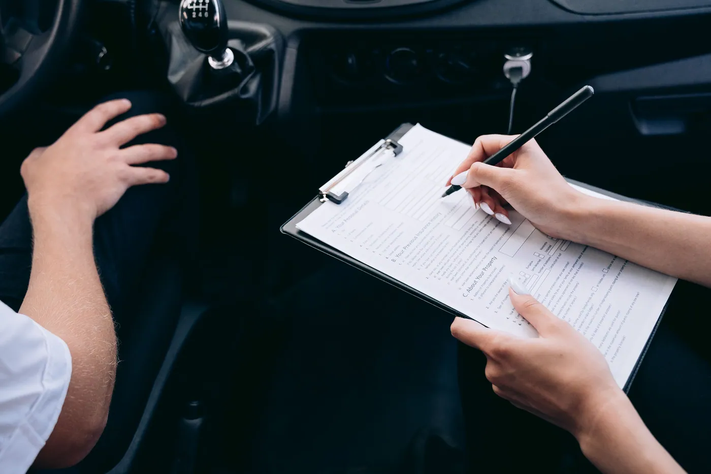 Two people going over paperwork on a clipboard inside a car.